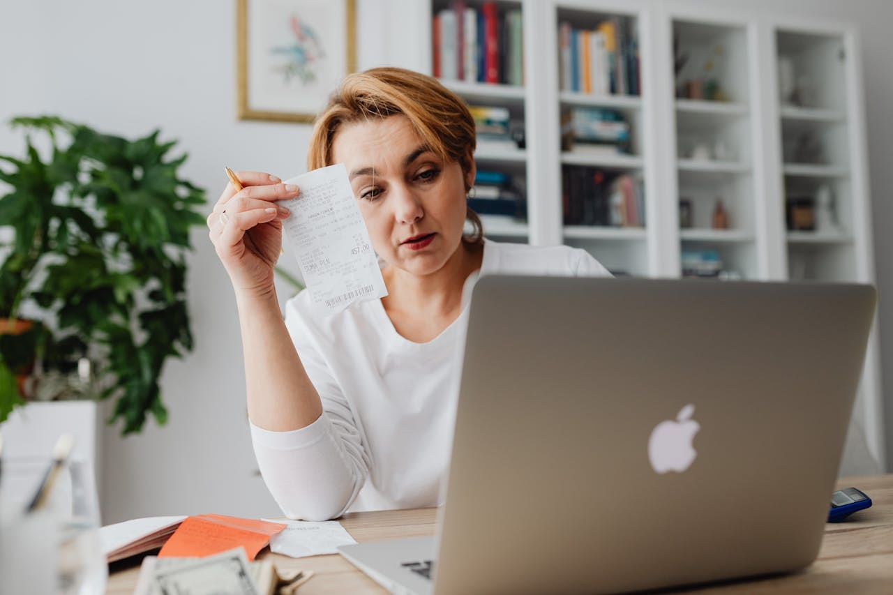 Woman concentrating on receipts while using a laptop, reflecting financial stress.