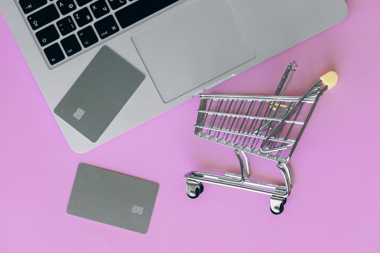 A minimalist flat lay of a credit card, laptop, and miniature shopping cart.